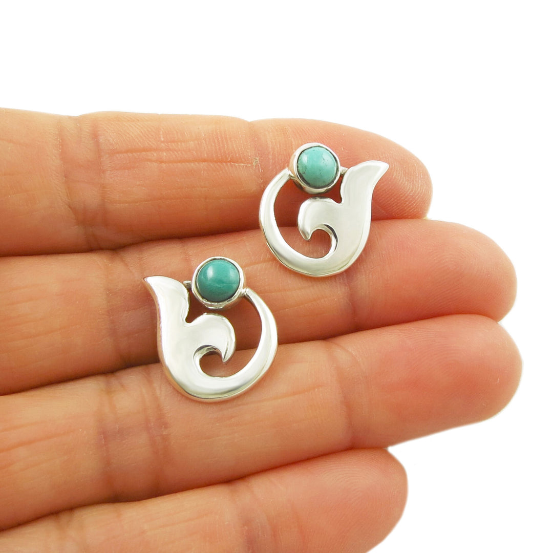 A pair of silver calla lily earrings with turquoise gemstone beads, held in a person's hand.