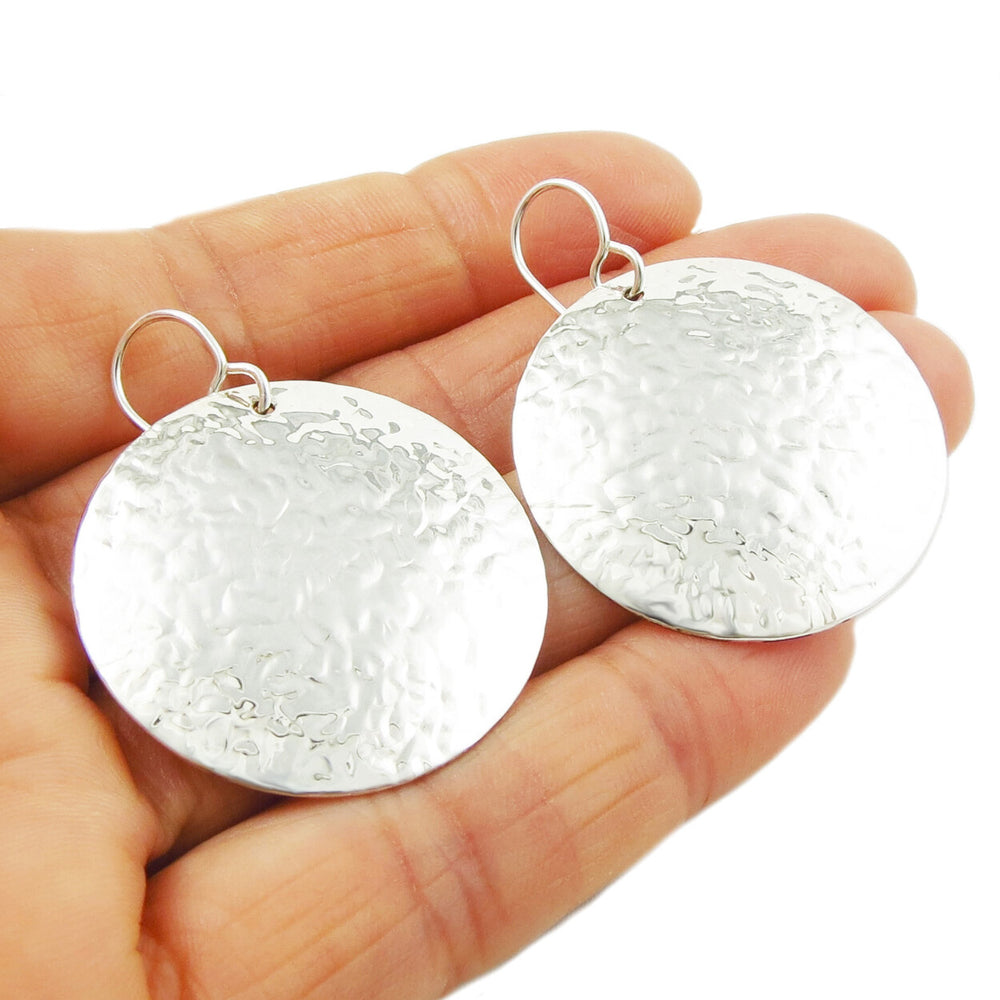 Large hammered sterling silver earrings held in a person's hand on a white background