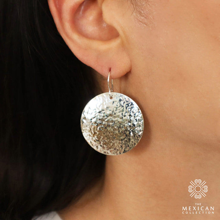 Large hammered silver circle disc earrings worn by a woman with dark hair