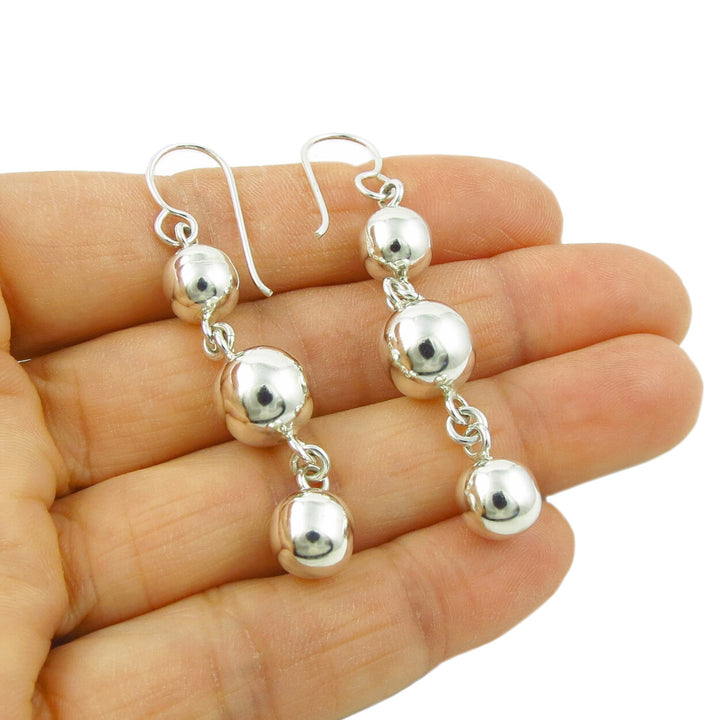 Long sterling silver triple ball bead drop earring held in a person's hand
