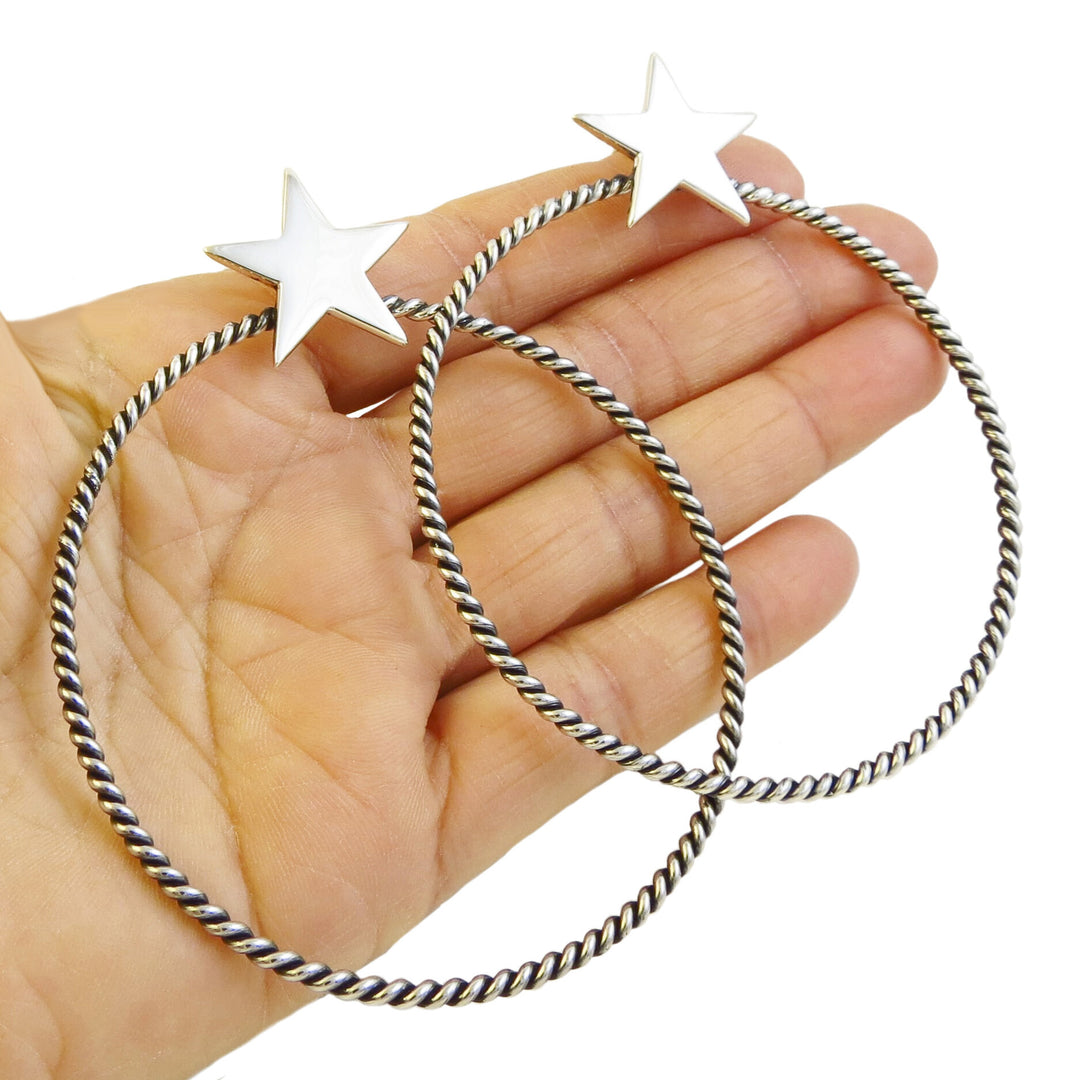 Sterling silver twisted hoop earrings with polished stars held in a person's hand.