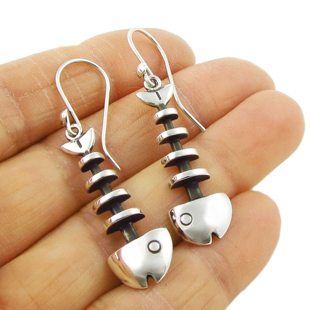 Maria Belen Nilson designer silver fish skeleton earrings held in a person's hand.
