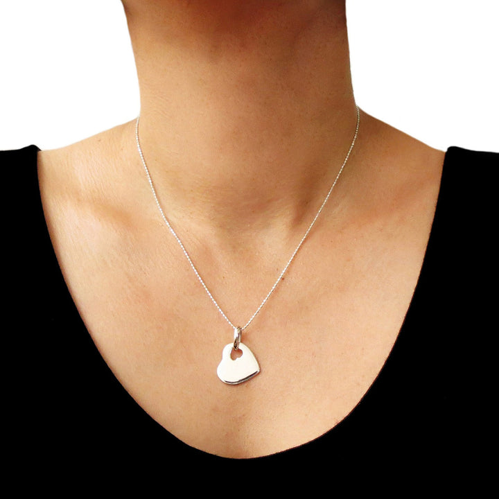 A person wearing a silver heart tag pendant necklace with a sleek curb chain.