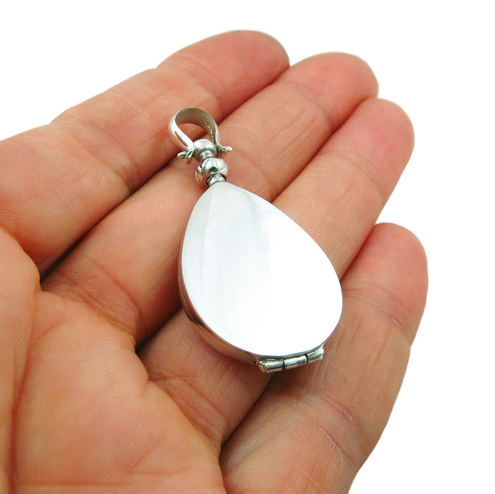 A sterling silver oval locket pendant held in a person's hand, with a screw mechanism on the bale for opening the locket.