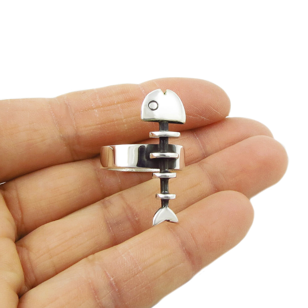 A hand-crafted silver fish skeleton ring by Maria Belen Nilson, with a polished and blackened finish, displayed on a person's hand.