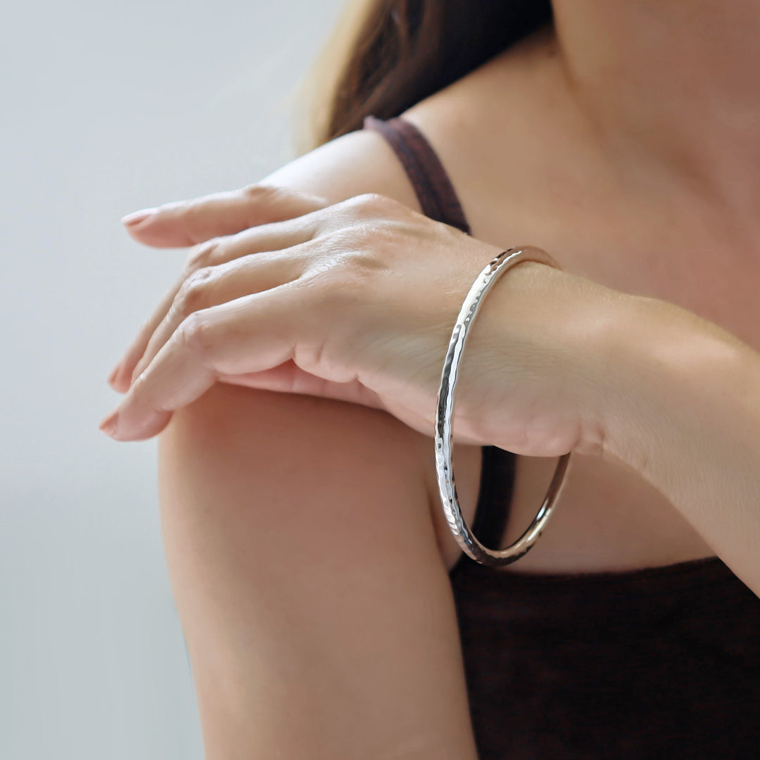 Hammered silver bracelet on a person's wrist with a neutral background