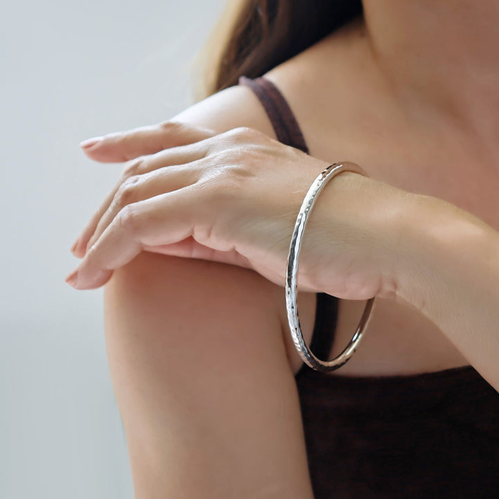Hammered silver bracelet on a person's wrist with a neutral background