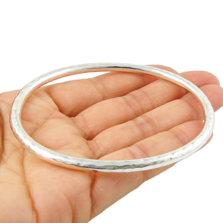Oval silver bangle on a hand against a white background