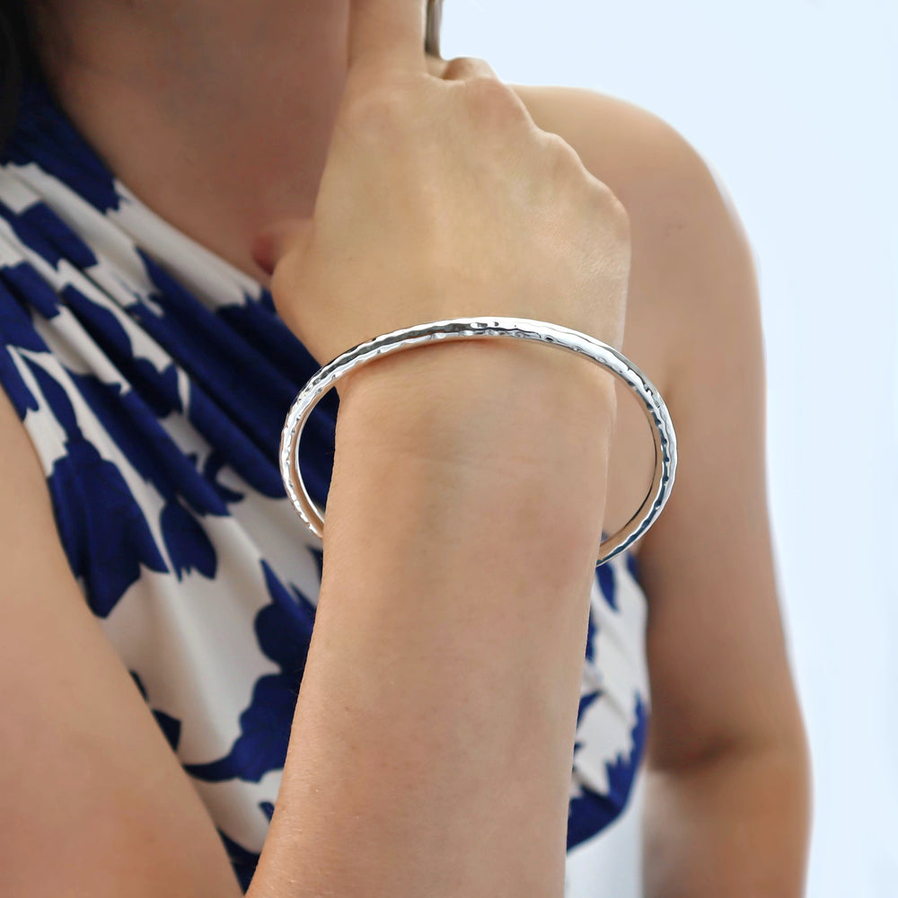 Hammered oval silver bangle on a woman's wrist with a blurred background