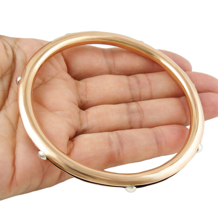 A large polished copper tube bangle jewellery for women with 925 silver accents held in a perosn's hand. 