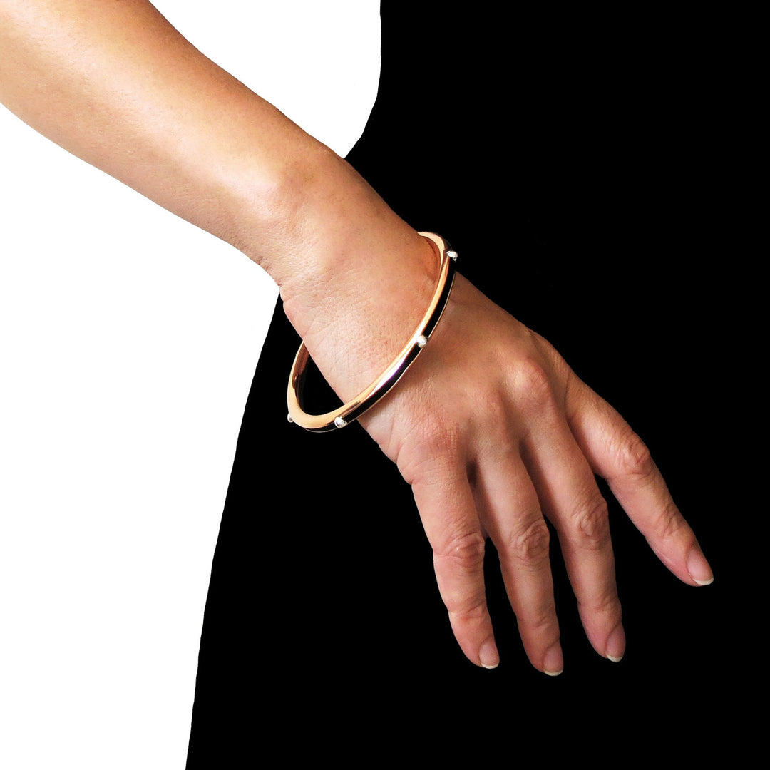 A large polished copper circle bangle with  25 silver accent worn by a woman in a black dress. 