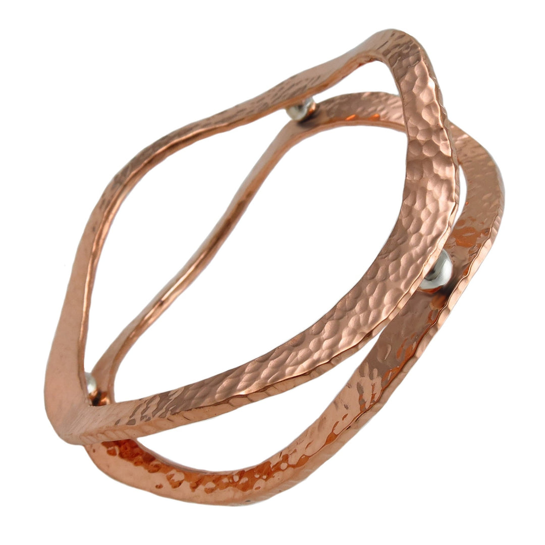A large handmade hammered copper and 925 silver statement bangle for women on a white background