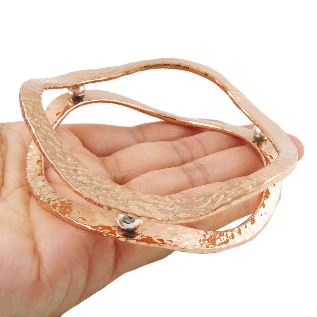 A large two tone copper and silver Mexican handmade bangle held in a hand against a white background