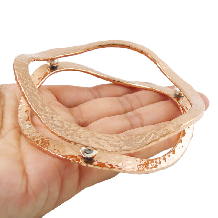 A large two tone copper and silver Mexican handmade bangle held in a hand against a white background