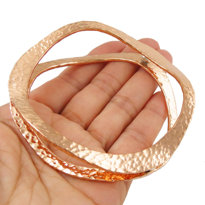 Large hammered copper double wave sculpted bangle for women held in a hand against a white background