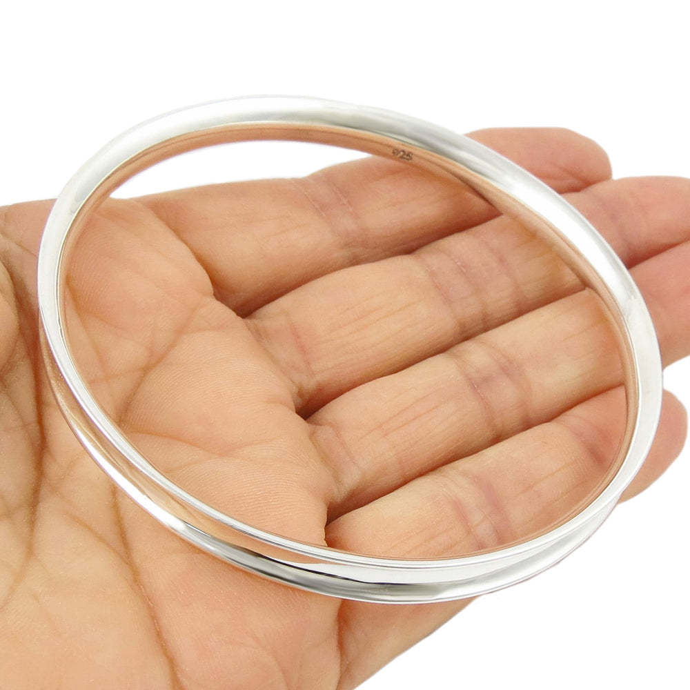 A large 925 heavy sterling silver circle bangle with a curved edge held in a person's hand. 