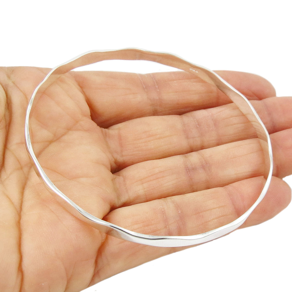 A large sterling silver circle bangle held in a person's hand. 