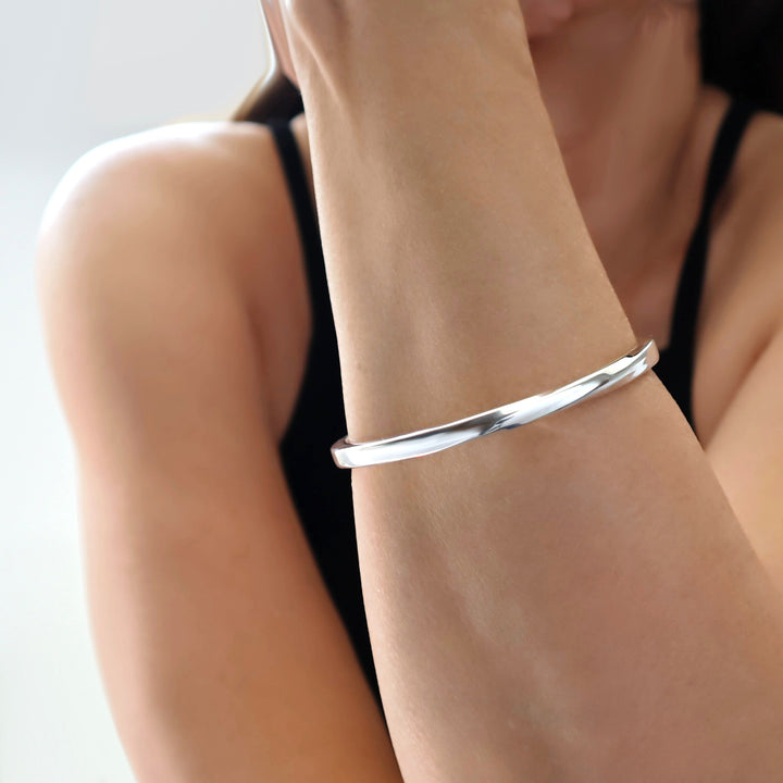 Sterling silver twisted circle bangle bracelet on a person's wrist with a neutral background