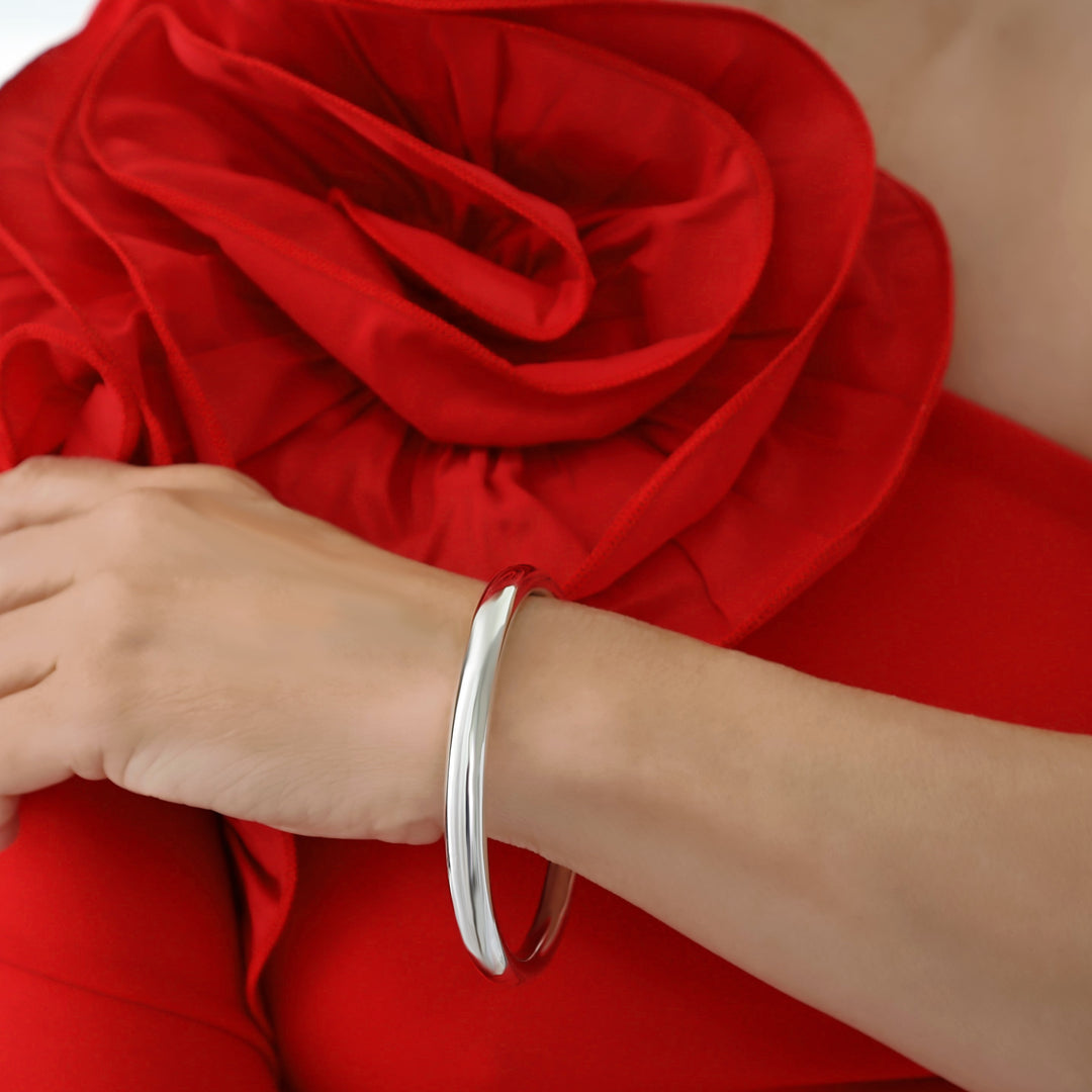 A woman in a red dress with a large floral detail wearing a wide sterling silver tube bangle on her wrist. 