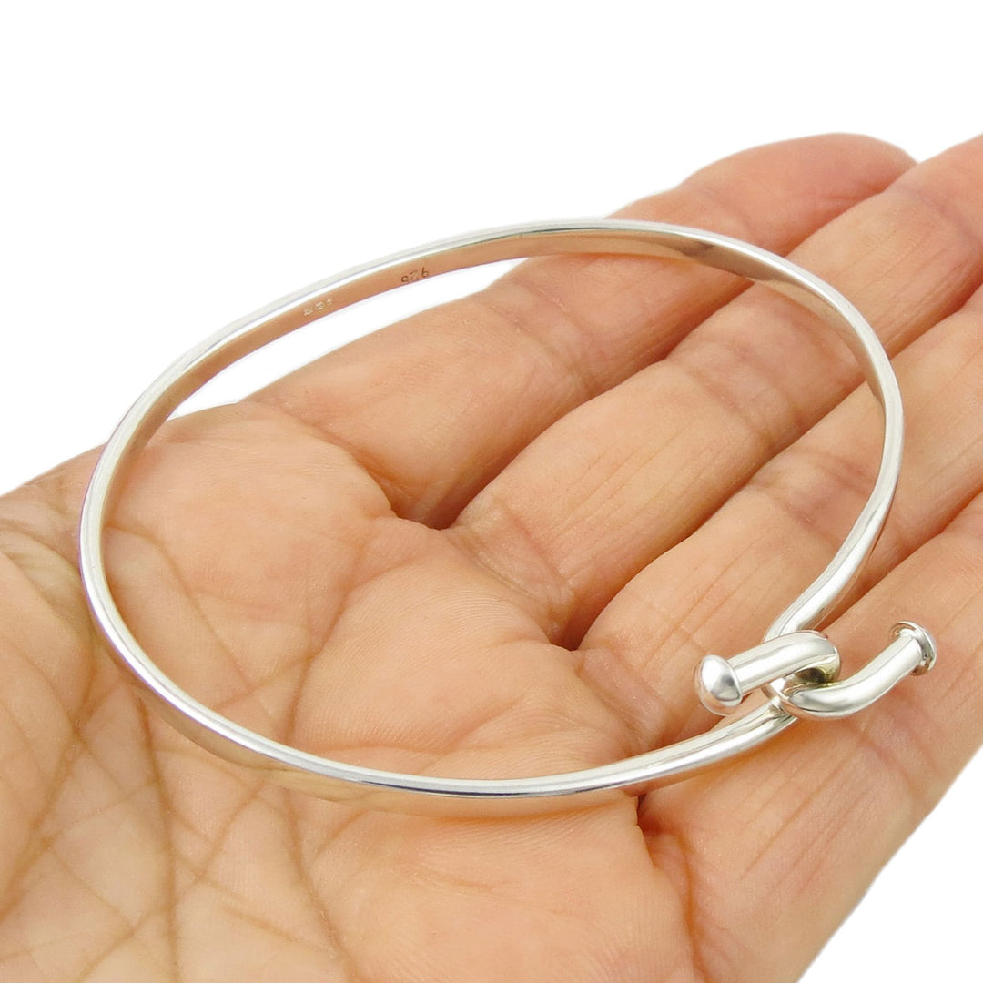 A front hook sterling 925 silver ovall bangle held in a perosn's hand on a white background. 