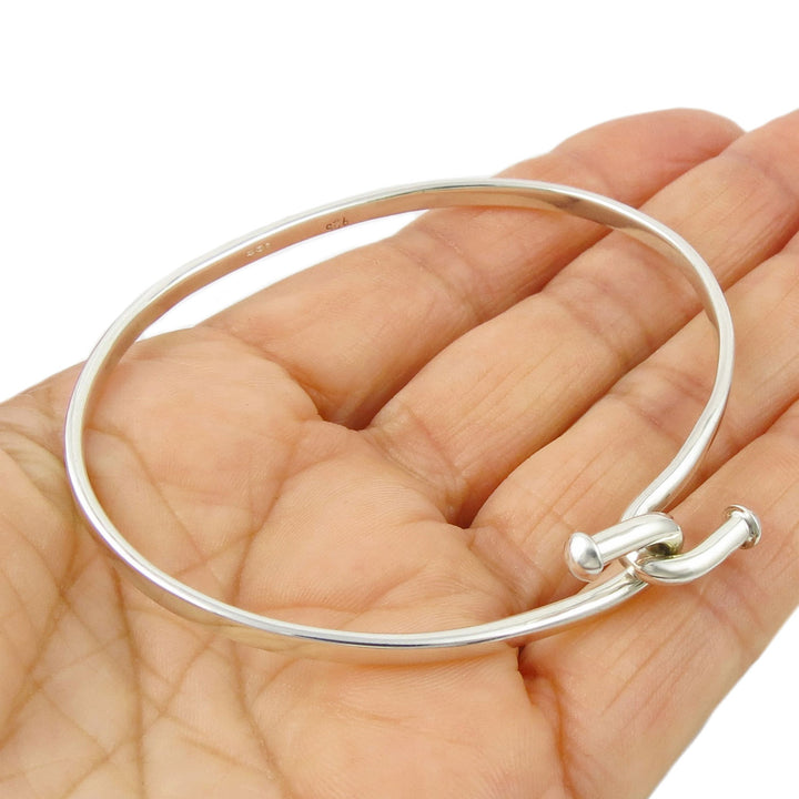 A front hook sterling 925 silver ovall bangle held in a perosn's hand on a white background. 