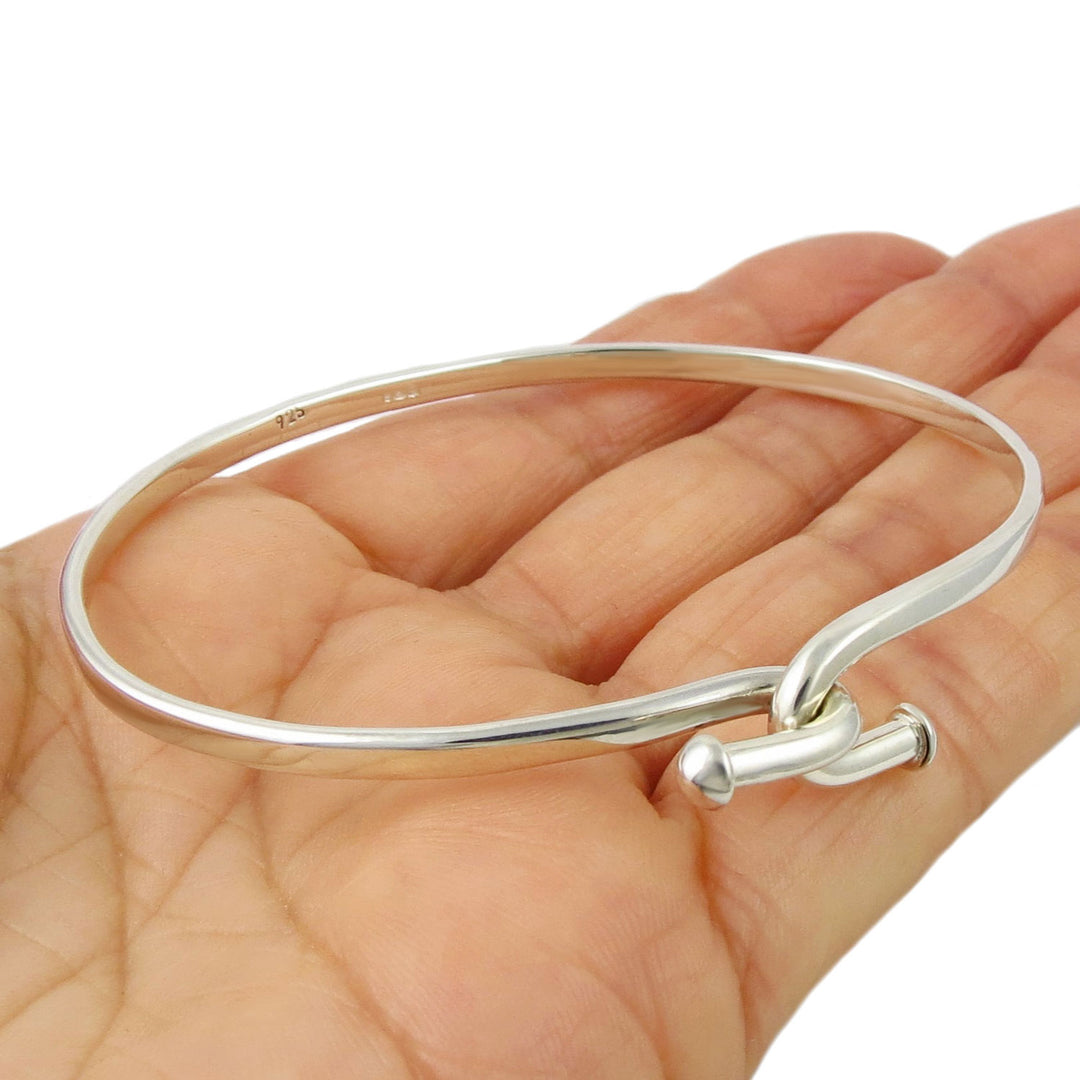 Sterling 925 silver oval bangle with a knot hook design on the front held in a hand on a white background