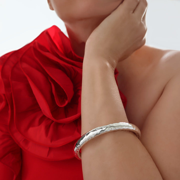 A woman in a red dress wearing a chunky sterling silver tube bangle with a hammered finish. 