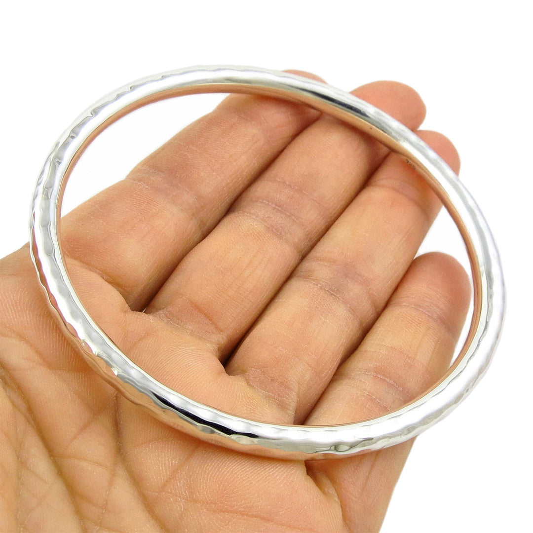 LLarge sterling 925 silver bangle with a hammered finish on a hand against a white background