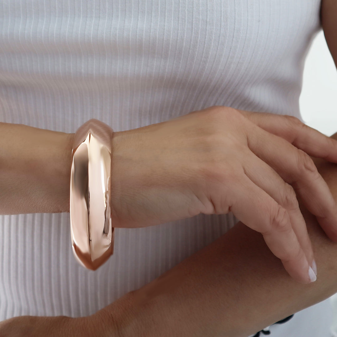 Large polished copper bangle worn by a person with a white top.