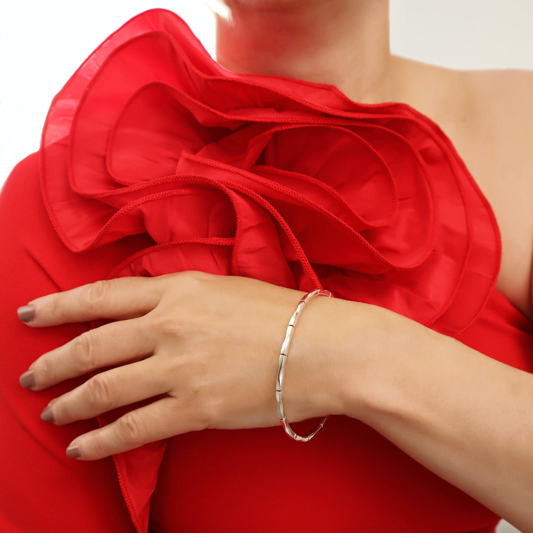 Woman in a red dress with a large floral shoulder detail wearing a unique handmade UK 925 sterling silver bangle with a hand carved bamboo pattern. 