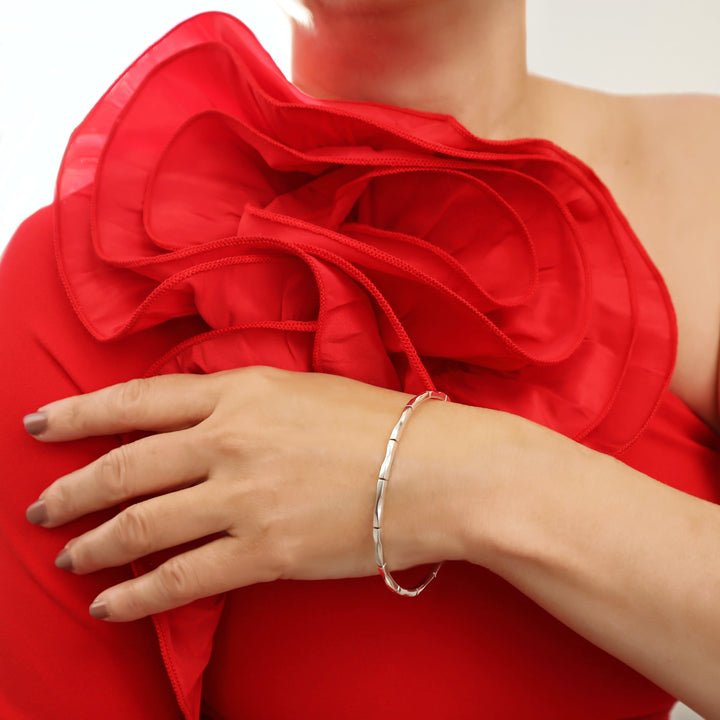 Woman in a red dress with a large floral shoulder detail wearing a unique handmade UK 925 sterling silver bangle with a hand carved bamboo pattern. 