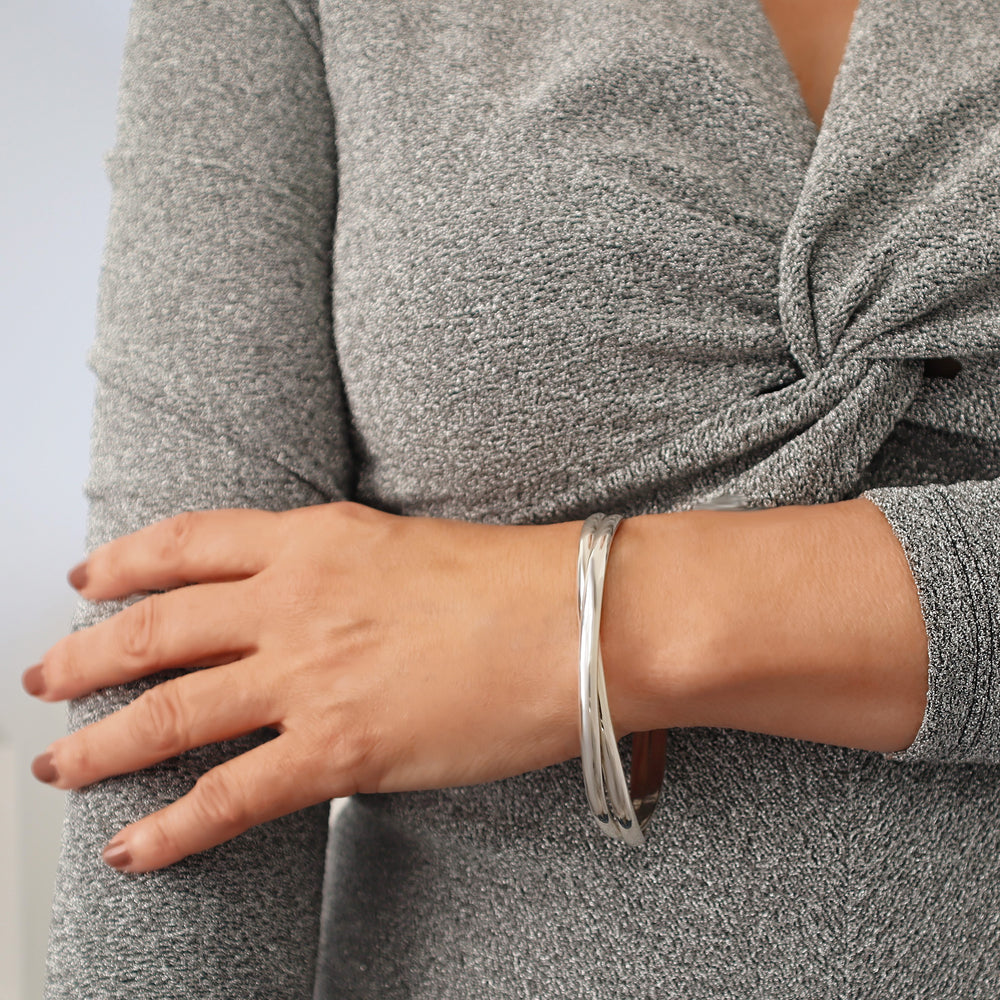 Woman wearing a large oval sterling silver double interlocking bangle on a plain background