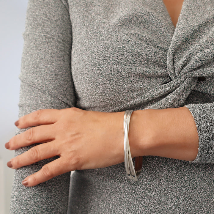 Woman wearing a large oval sterling silver double interlocking bangle on a plain background