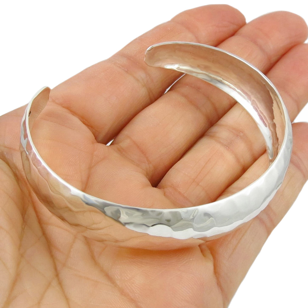 A wide sterling silver bracelet cuff with a hammered finish held in a person's hand. 