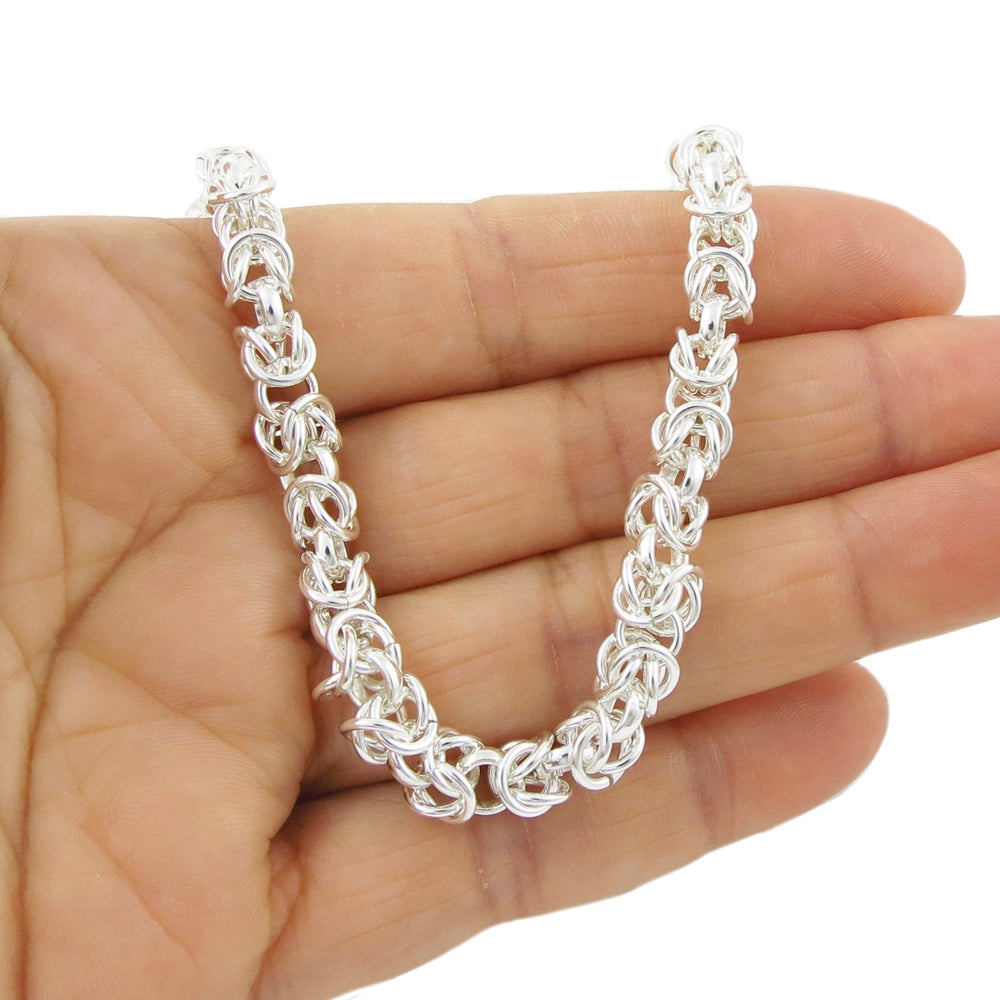 A sterling silver Byzantine chain bracelet held in a hand, displaying its intricate design of interlocking rings.