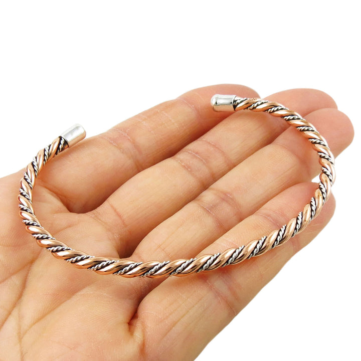 Two tone copper and 925 silver braided rope bracelet cuff on a woman's hand against a white background