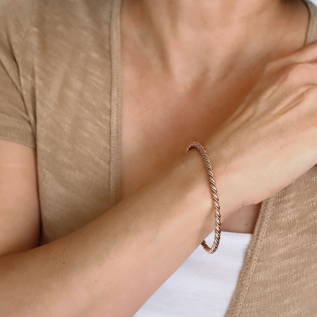 Close-up of a woman wearing a two tone 925 silver and copper rigid bracelet on a neutral background