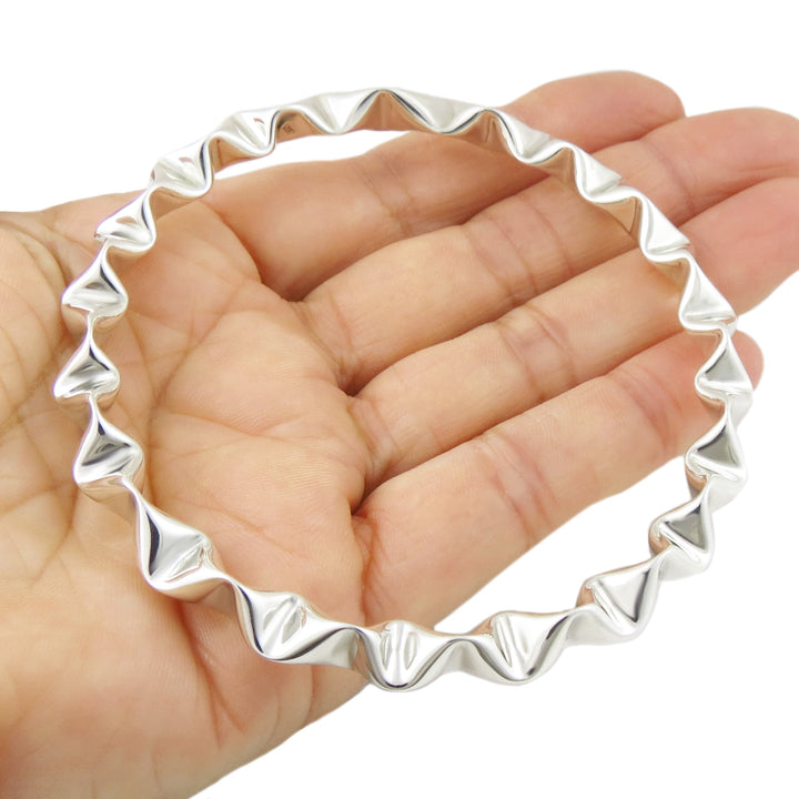 Polished 925 sterling silver bracelet bangle with wavy design on a hand against a white background