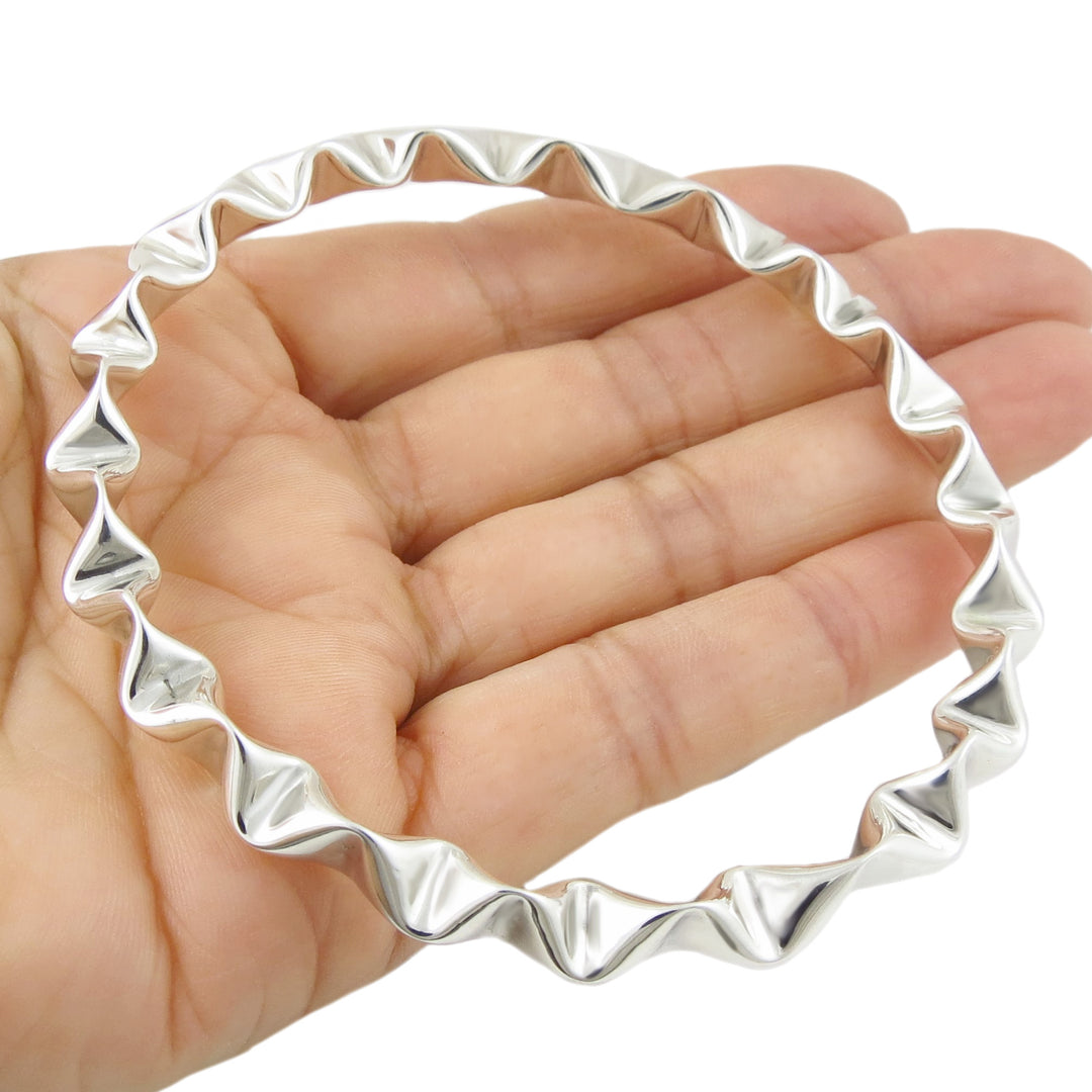 Sterling 925 silver bangle with unique crimped wavy design held in a hand on a white background