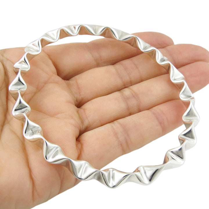Sterling 925 silver bangle with unique crimped wavy design held in a hand on a white background