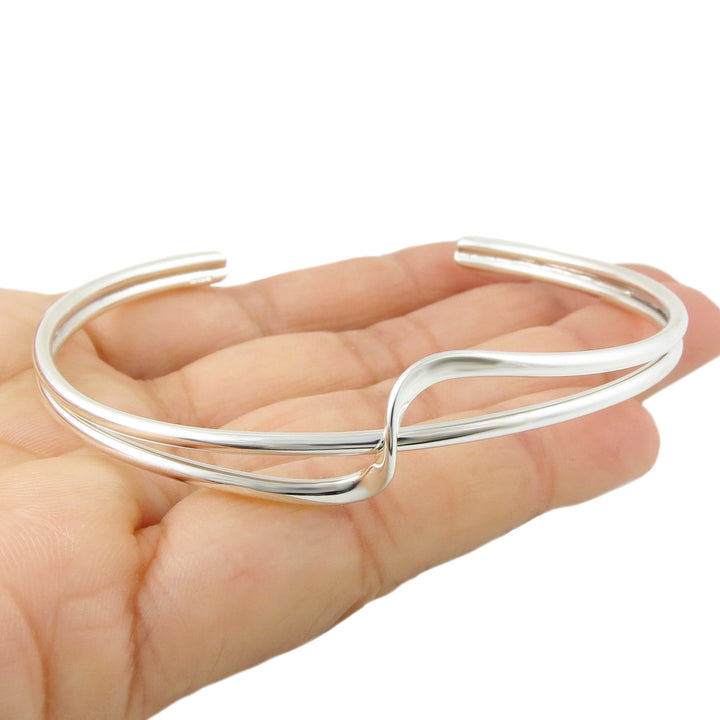 Silver bracelet cuff with a twist accent at the front on a hand against a white background