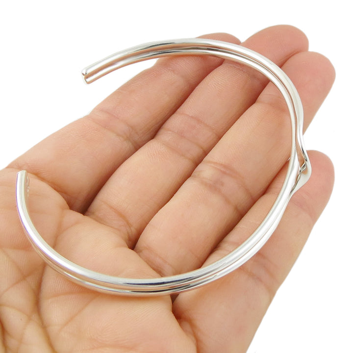 Silver bangle bracelet held in a hand on a white background
