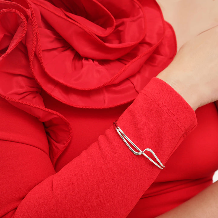 A woman in a ed dress with a large floral accent wearing a sterling silver bracelet cuff with a curve detail on the front. 