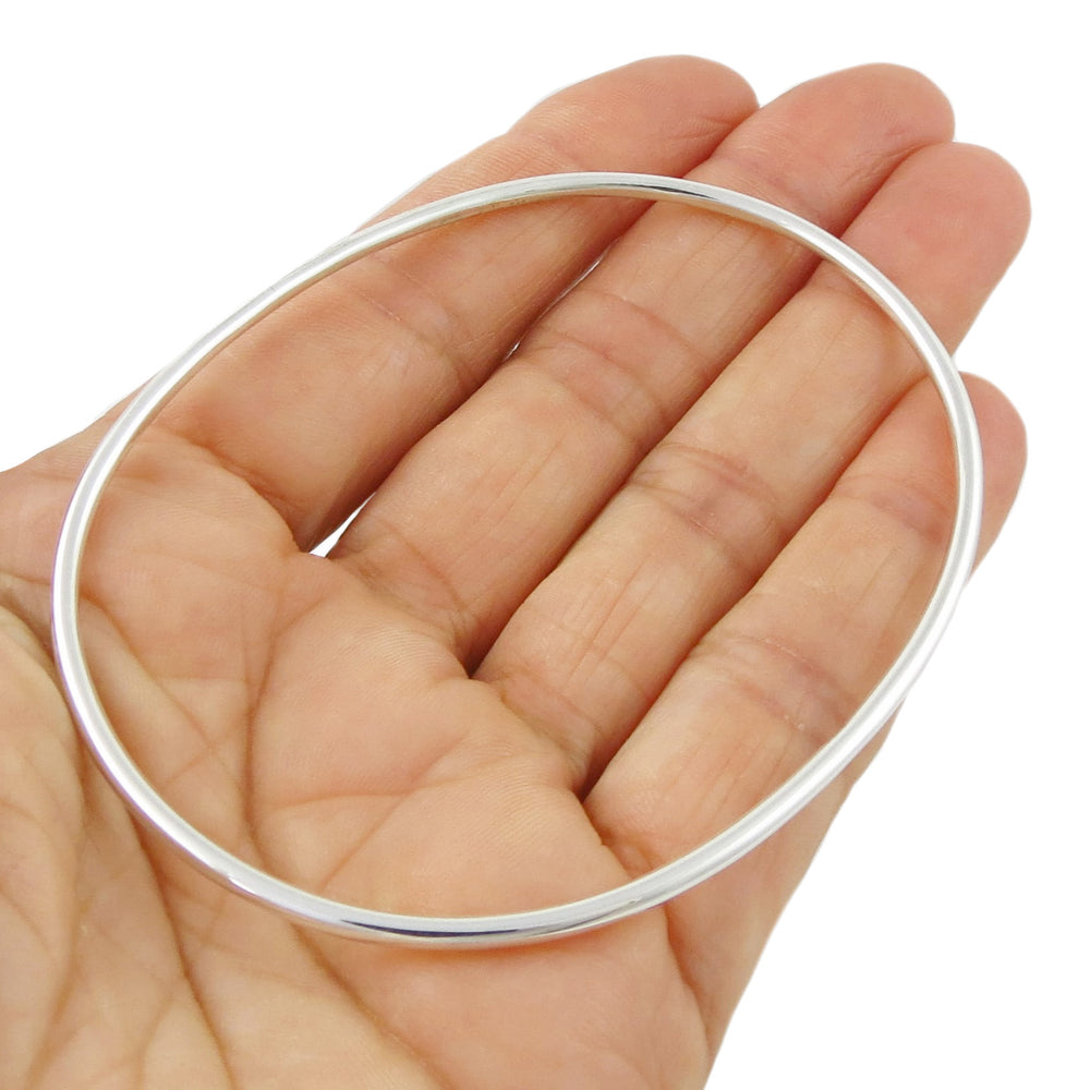 A large oval bangle with a rounded edge handmade from solid 925 sterling silver held in a person's hand