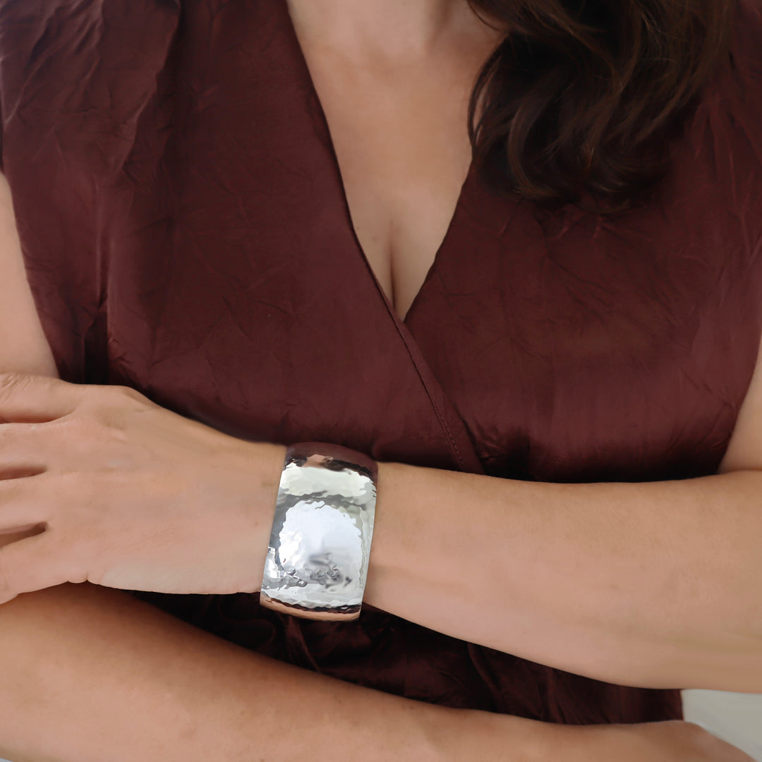 Hammered wide bracelet cuff in hallmarked sterling 925 silver worn by a woman in a brown silk dress. 