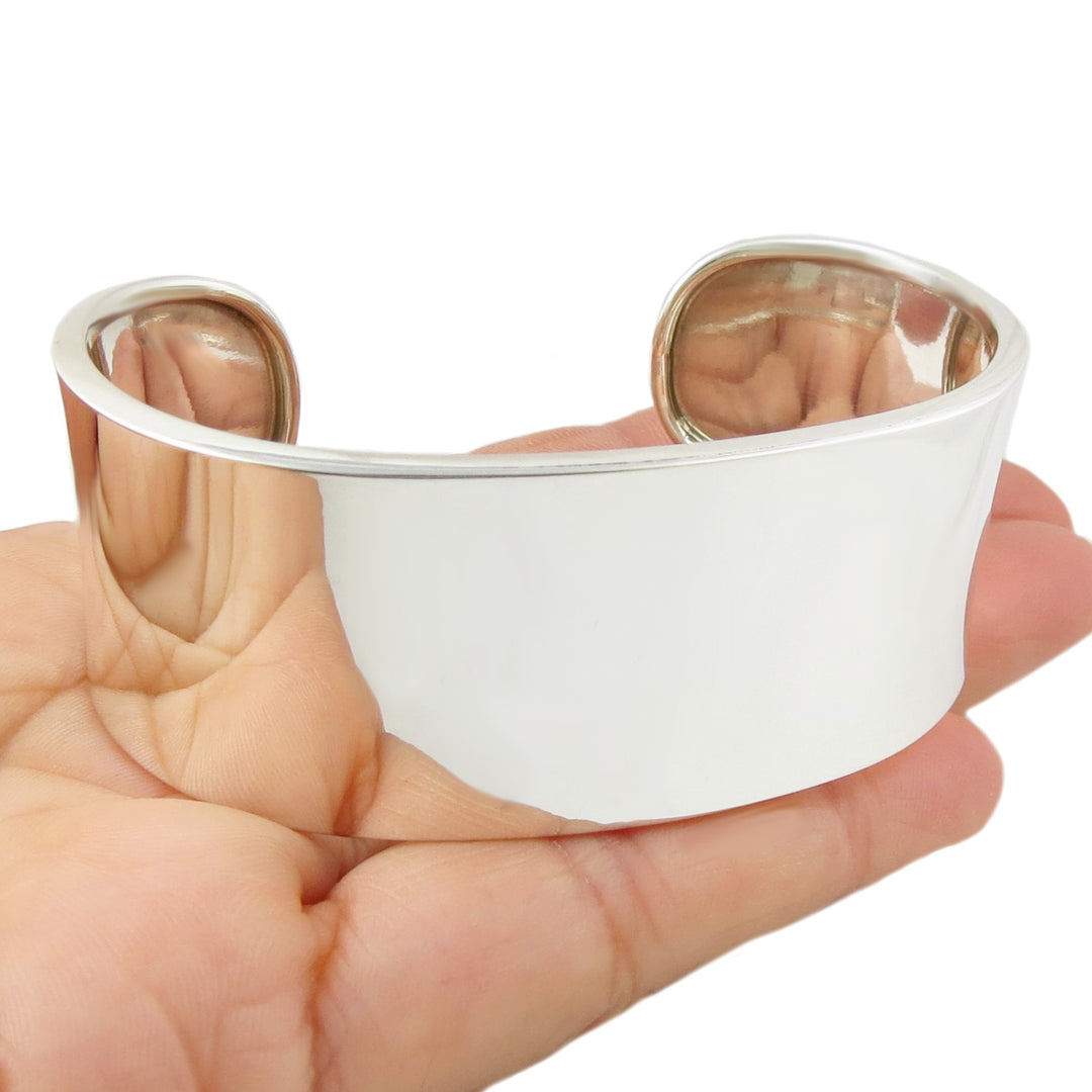 A large sterling silver cuff bracelet with a polished finish held in a person's hand. 