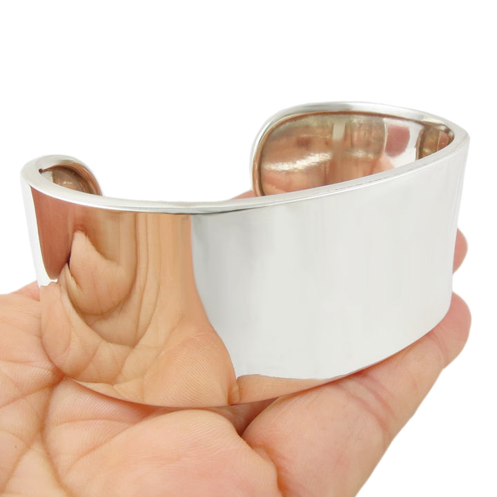 A wide polished silver cuff bracelet held in a person's hand. 