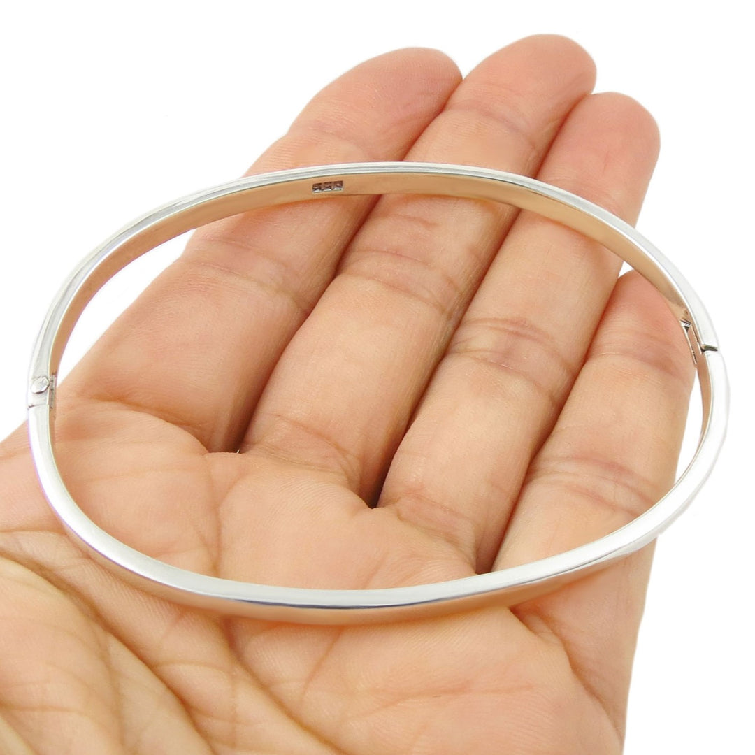 A large oval sterling 925 silver hinged bangle bracelet held in a persons hand on a white background. 