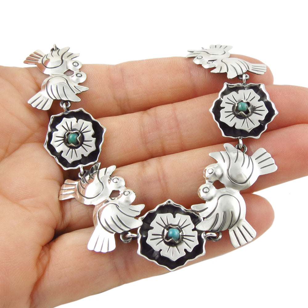 Silver earrings with floral designs and turquoise stones held in a hand against a white background