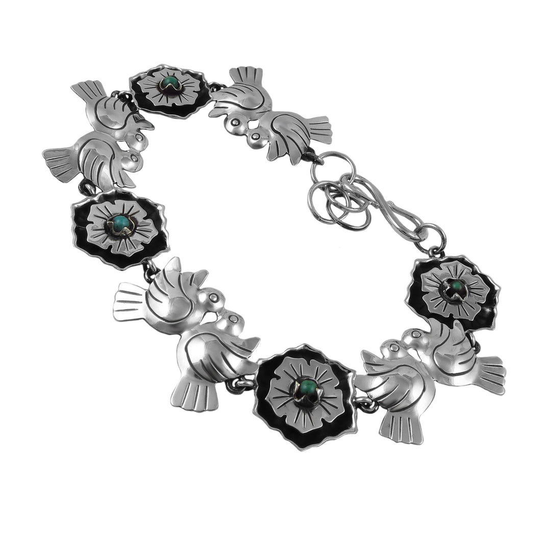Silver bracelet with turquoise gemstones, lovebird and flower designs on a white background